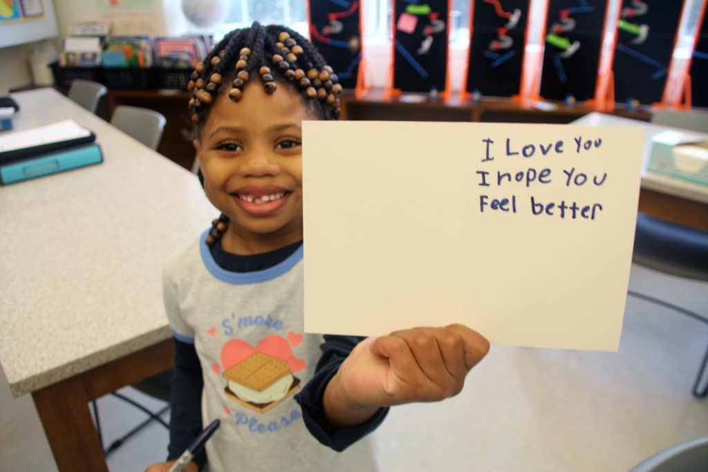 Lower School child shows card for cancer patients